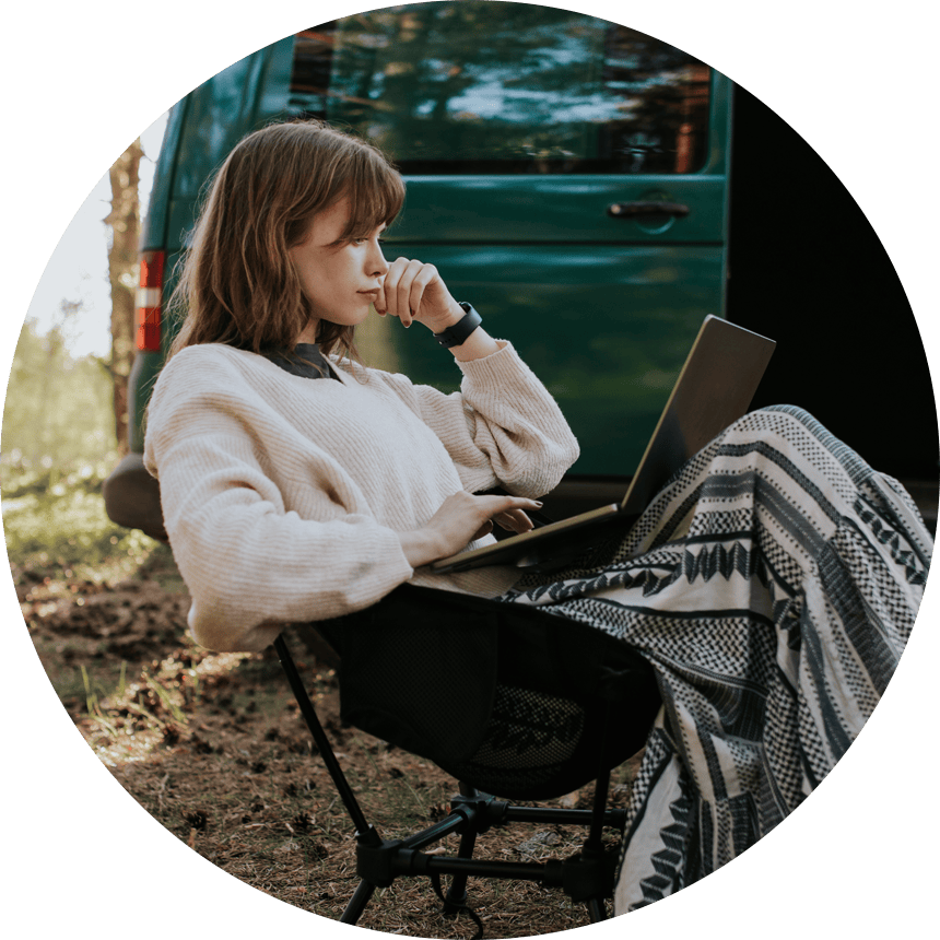 Žena pracující na notebooku v přírodě u obytné dodávky – buďte online odkudkoliv díky doménám a webhostingu od Active24