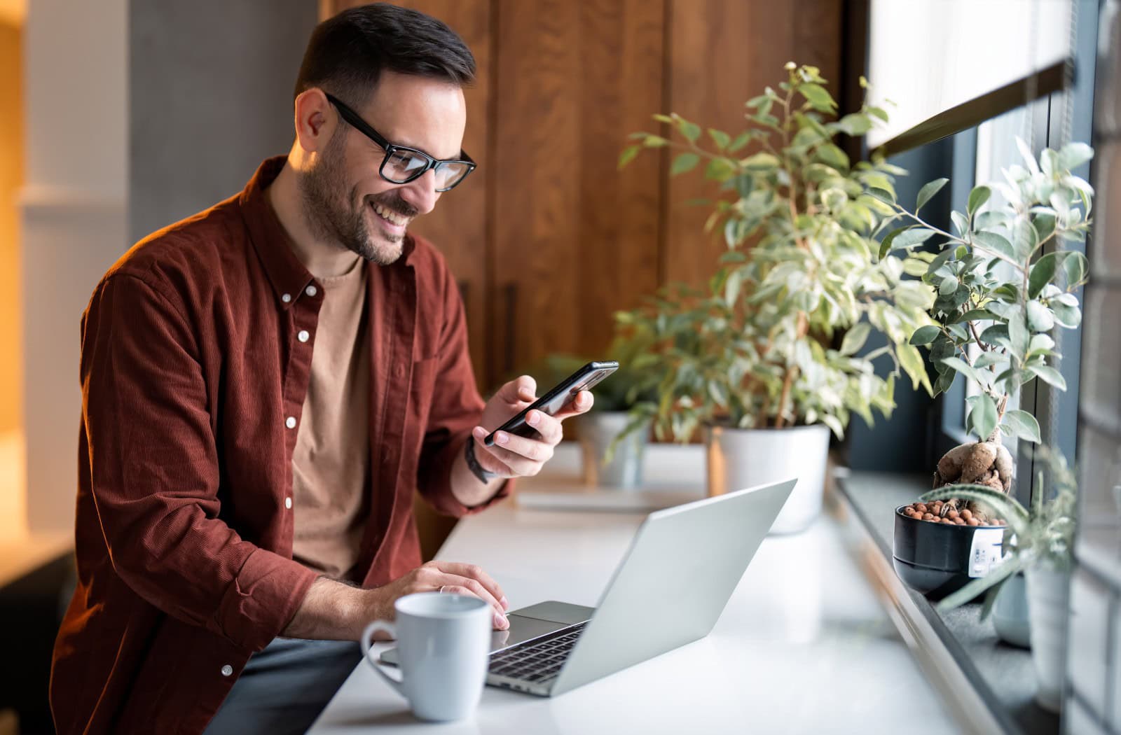 Muž pracuje na notebooku a zároveň sleduje mobilní telefon. – bezstarostná správa webu díky spolehlivému webhostingu a doménám od Active24